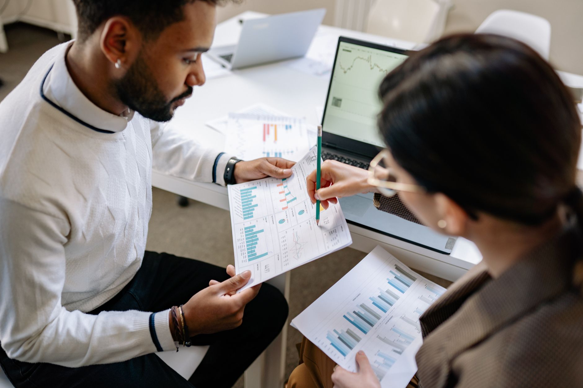 Two colleagues review charts and dashboards together at an office table.