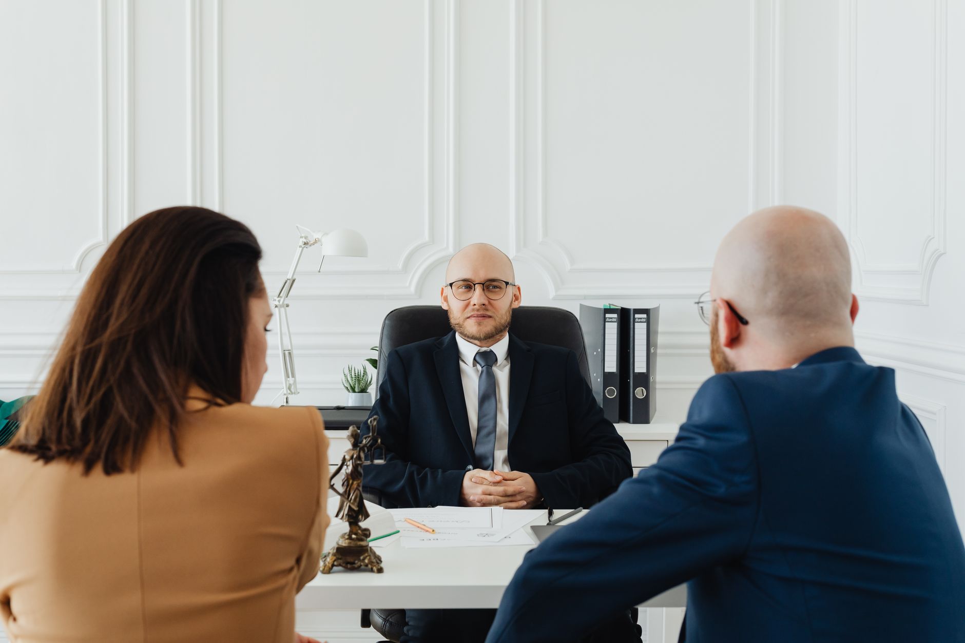 An attorney meets with two clients across a desk in a law office.