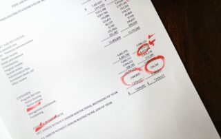 Financial report page marked with red handwritten annotations on wooden desk surface