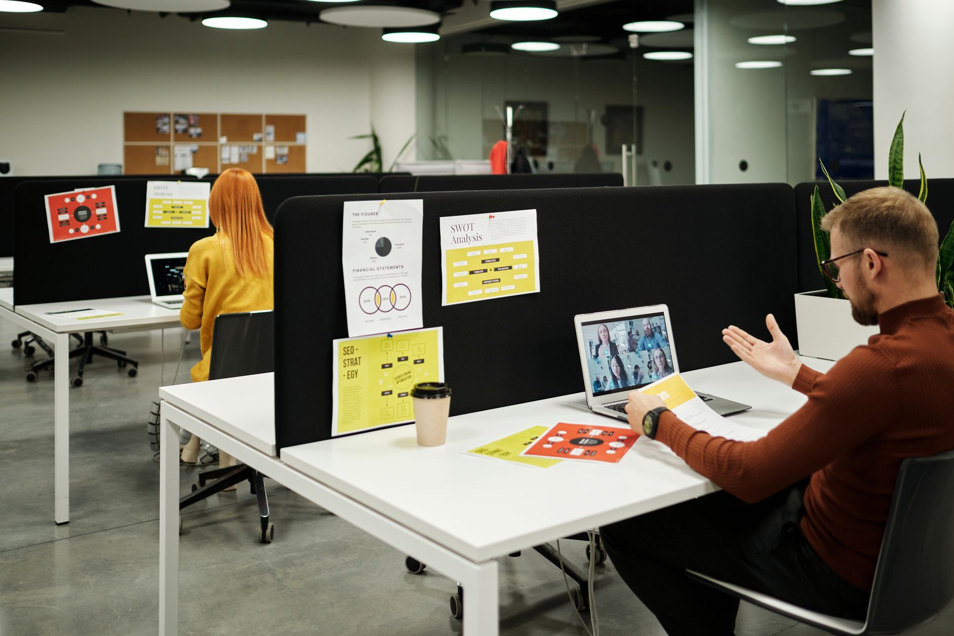 Colleagues collaborate over laptops and a video call in a modern office.