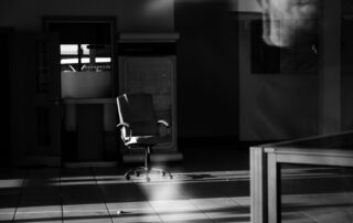 Black-and-white photo of a single empty chair in a dim office space.
