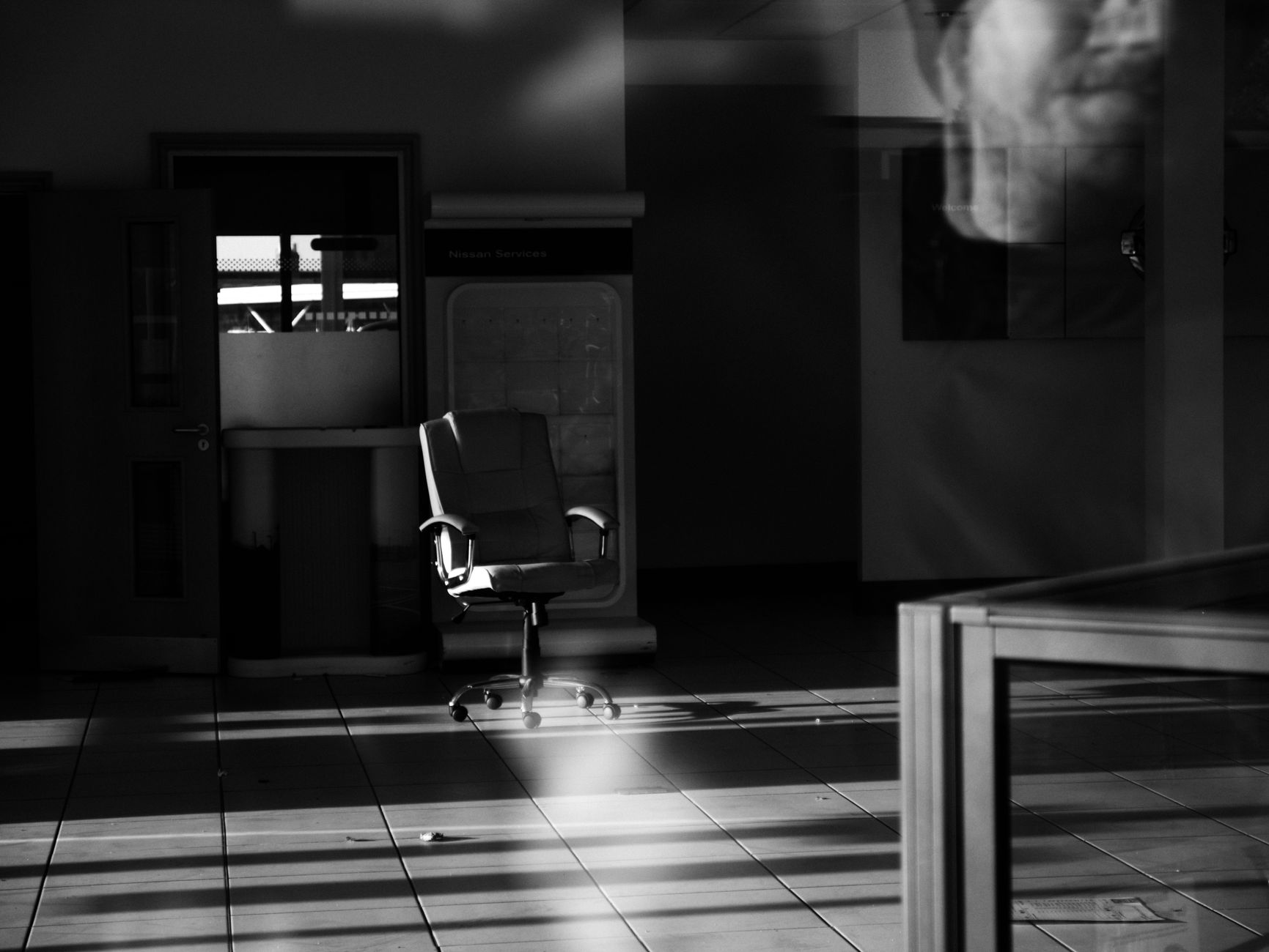 Black-and-white photo of a single empty chair in a dim office space.