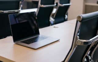 Open laptop alone on wooden conference table with empty black chairs