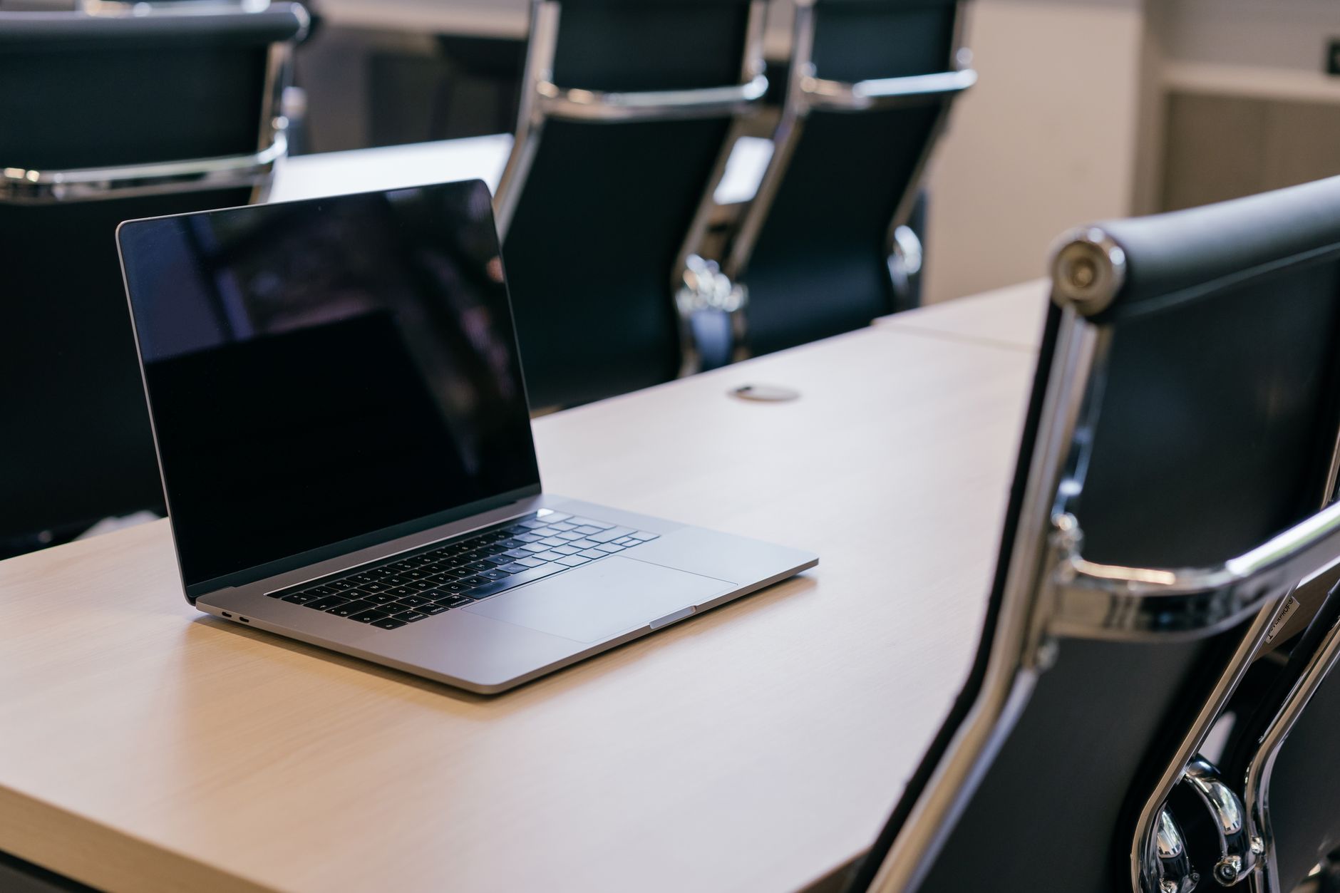 Open laptop alone on wooden conference table Open laptop alone on wooden conference table with empty black chairs