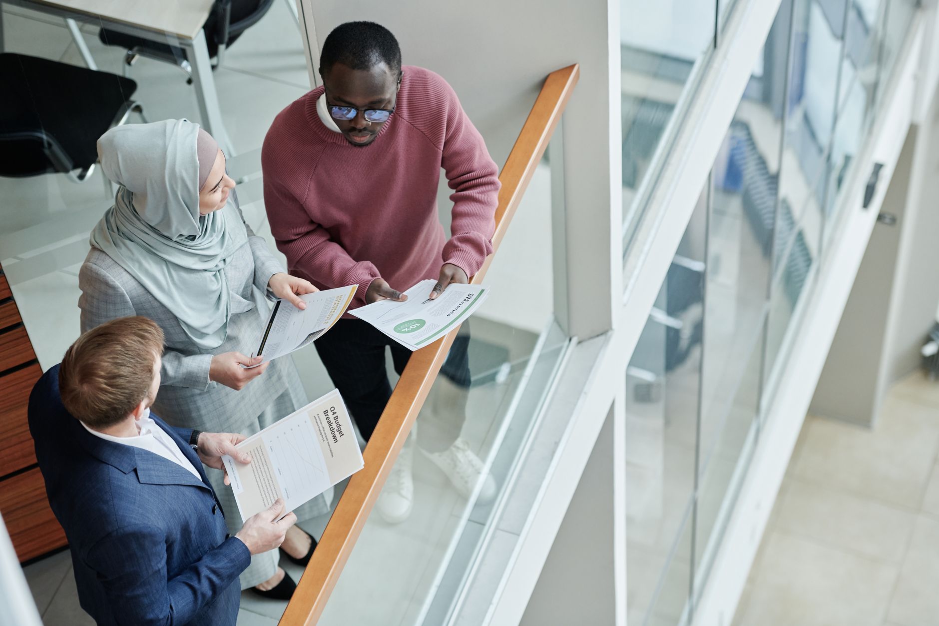 Three colleagues review shared documents together around a desk in a modern office.